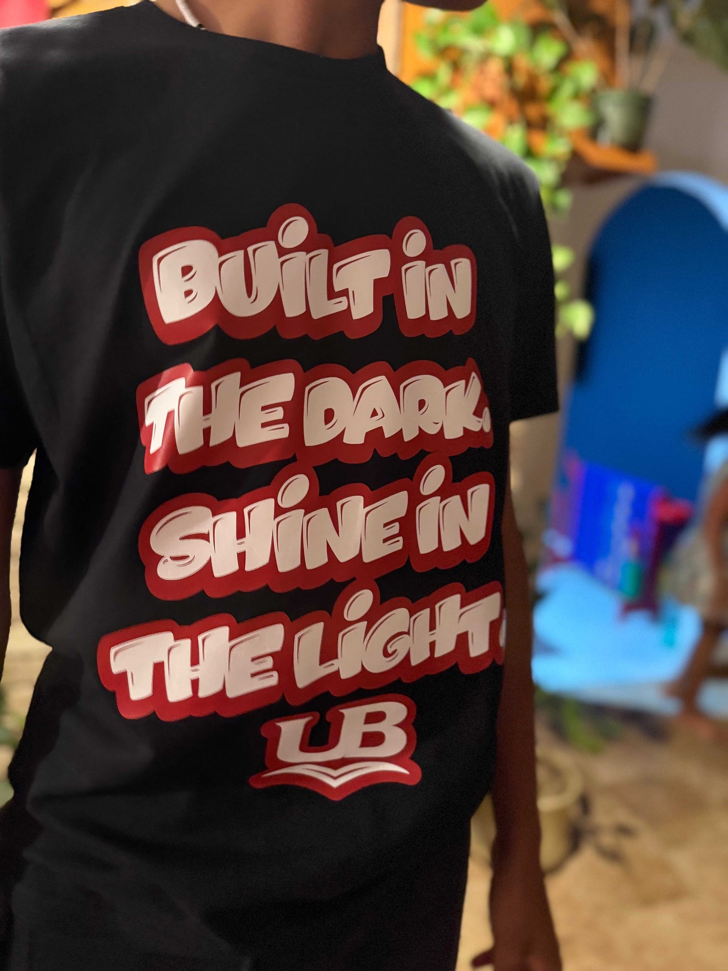 Black motivational streetwear t-shirt with red and white text reading Built in the Dark Shine in the Light by Underbrim